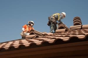 Two roofers install clay tiles on a roof